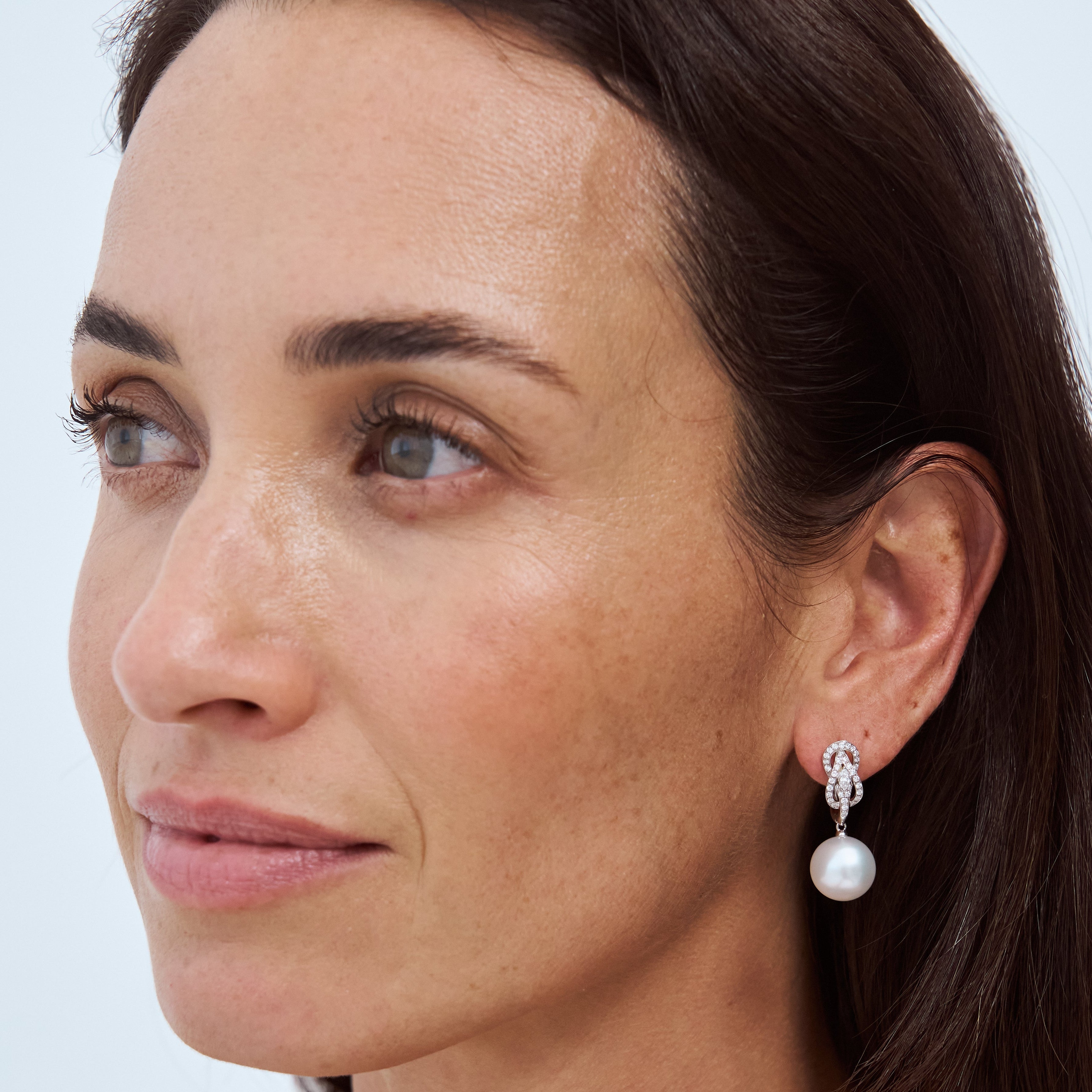 Model wearing Autore South Sea Pearls set in 18kt white gold white diamond Hercules Knot huggie earrings