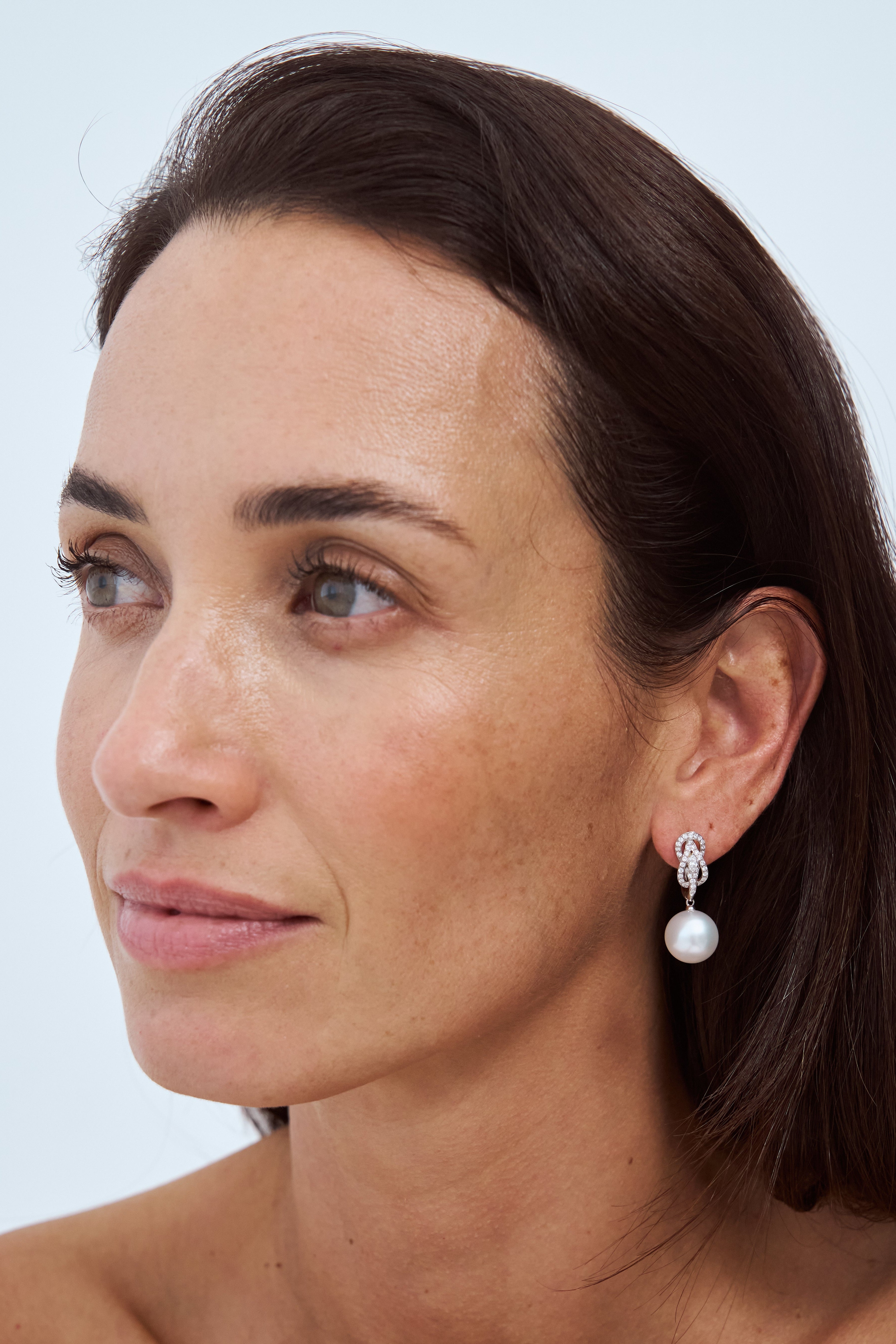Model wearing Autore South Sea Pearls set in 18kt white gold white diamond Hercules Knot huggie earrings